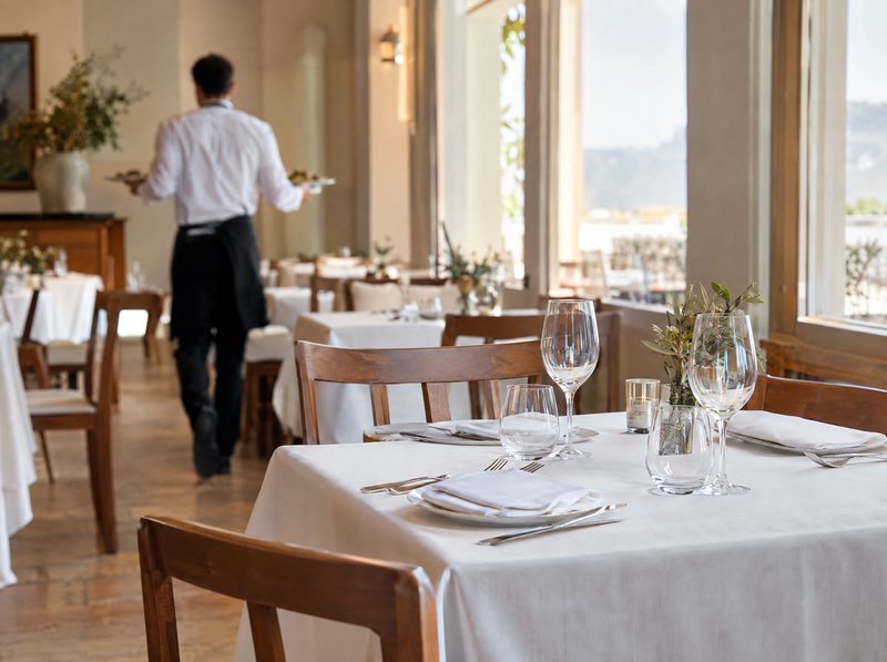 Comedor de restaurante a mediodía con las mesas puestas y un camarero al fondo